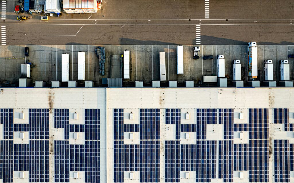 Aerial view: Several trucks are driving toward a building whose roof is equipped with solar panels.