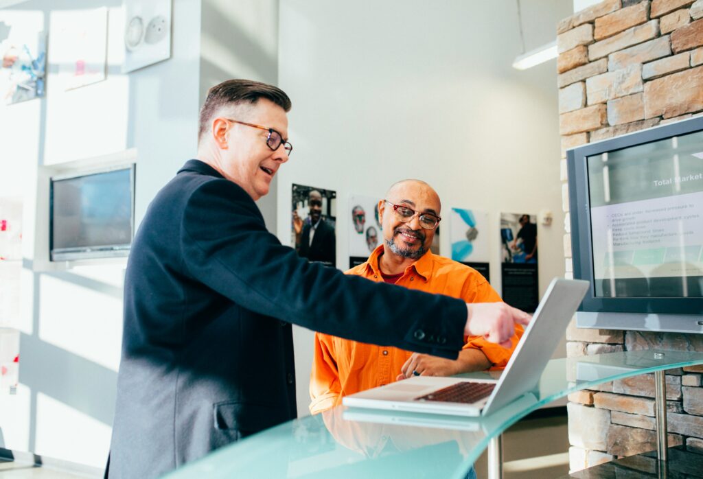 Two people are having a conversation while one person is showing something to the other on a laptop.