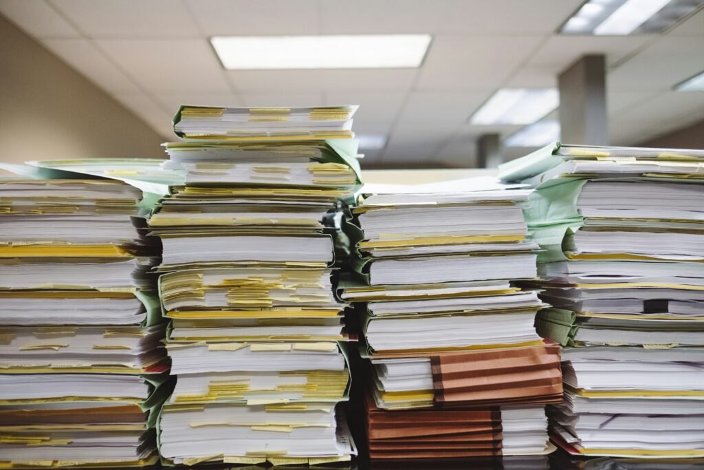 A table is covered with several tall stacks of papers and documents.